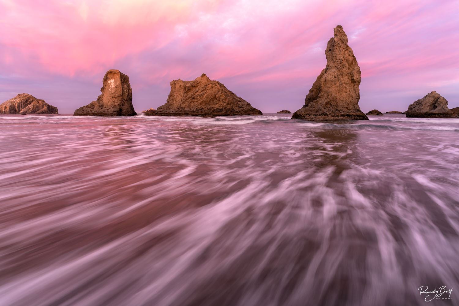 Coastal scene with large ocean rocks at sunrise or sunset, water flowing around them